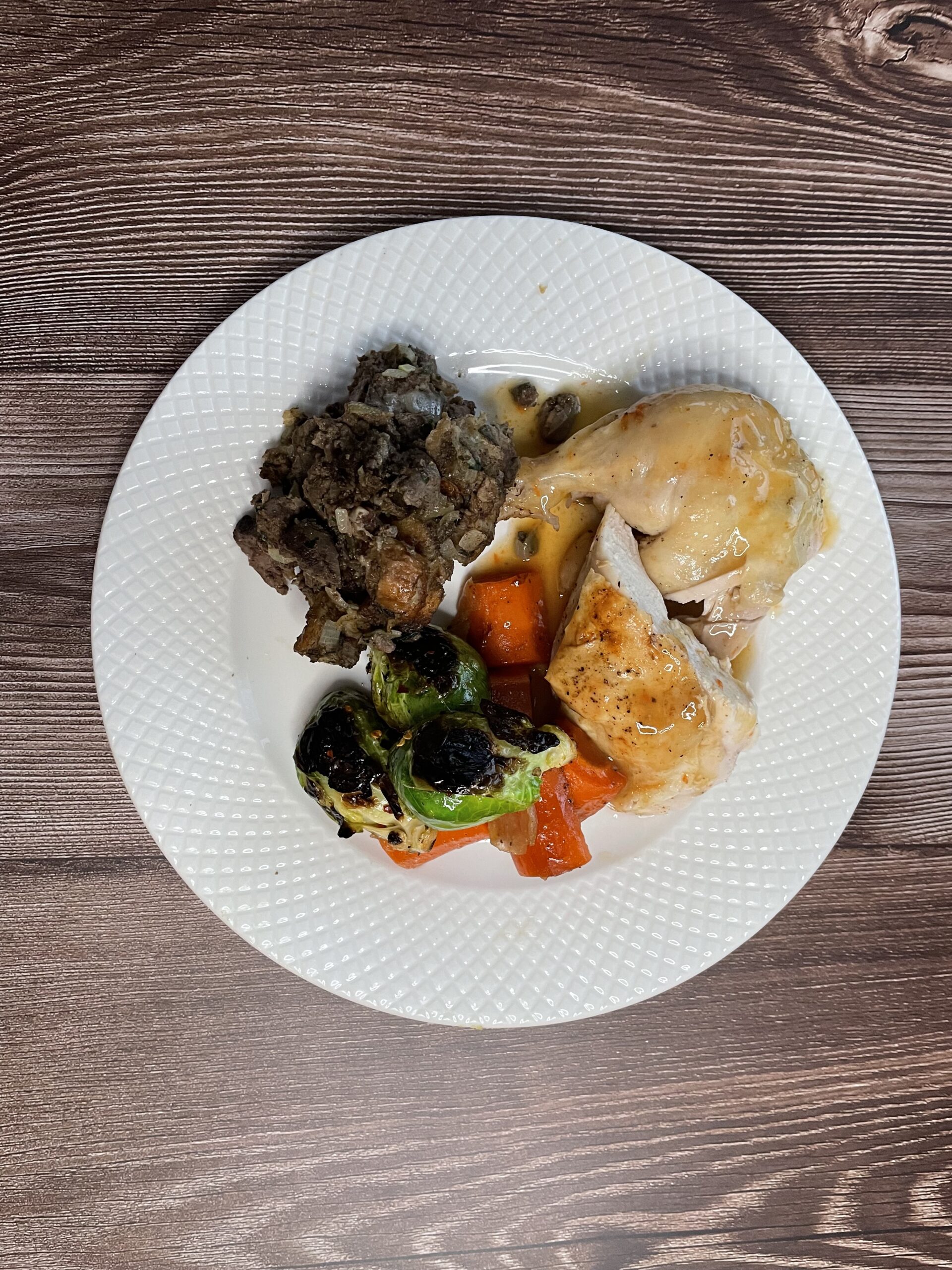 A dinner plate that contains a chicken leg and breast, roast veggies, fried Brussel sprouts, and an onion and sage dressing